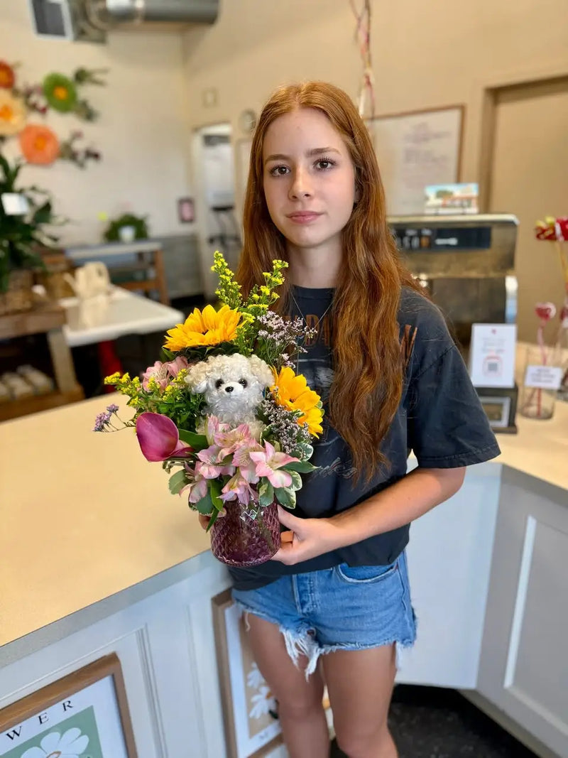 Person holding a bouquet of flowers and a teddy bear in a store setting